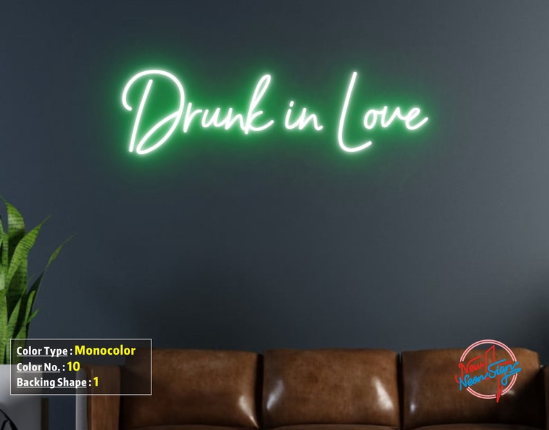 May include: Green neon sign with the text "Drunk in Love" on a dark gray wall. The sign is mounted above a brown leather couch.