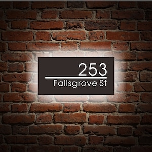 Puede incluir: Un letrero de n&uacute;mero de casa en blanco y negro con el n&uacute;mero 253 y el nombre de la calle Fallsgrove St. El letrero est&aacute; iluminado con una luz blanca.
