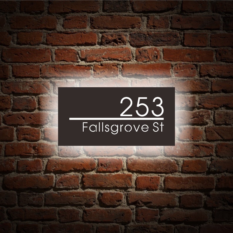 Puede incluir: Un letrero de n&uacute;mero de casa en blanco y negro con el n&uacute;mero 253 y el nombre de la calle Fallsgrove St. El letrero est&aacute; iluminado con una luz blanca.