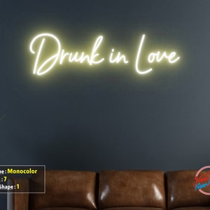 May include: A white neon sign with the text "Drunk in Love" on a dark gray wall. The sign is illuminated and casts a warm glow.