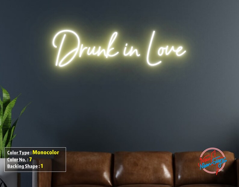 May include: A white neon sign with the text "Drunk in Love" on a dark gray wall. The sign is illuminated and casts a warm glow.