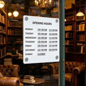 May include: A white rectangular sign with rounded corners and four grey mounting bolts displays opening hours in black text. The schedule lists Monday through Saturday with specific time slots and Sunday as closed, mounted on a glass door.