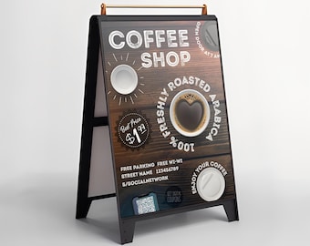 May include: A-frame sign for a coffee shop with a dark wood-grain background. The sign features the words "Coffee Shop" and "Freshly Roasted Arabica." A coffee cup with a heart-shaped design is in the center. The sign also includes a QR code.