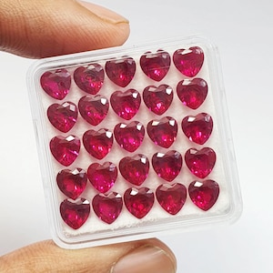 Può includere: Un contenitore di plastica trasparente pieno di gemme rosse sfaccettate a forma di cuore. Le gemme sono disposte in file e colonne. Il contenitore è tenuto da una mano.