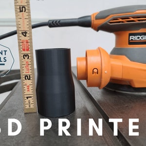 K&ouml;nnte beinhalten: Ein 3D-gedruckter schwarzer Kunststoffadapter f&uuml;r eine Ridgid-Schleifmaschine. Der Adapter ist 7,6 cm hoch und befindet sich neben einem Lineal.
