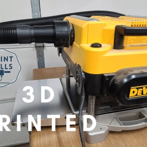 May include: A yellow DeWalt planer with a black dust collection hose attached. The planer is sitting on a wooden surface with a 3D printed metal plate in front of it. The text "PRINT MILLS" and "3D PRINTED" are visible in the image.
