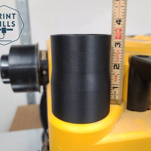 May include: A close-up of a black 3D printed dust collection adapter for a table saw. The adapter is 7.6 cm tall and is being measured with a ruler.