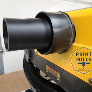 May include: Close-up of a black plastic exhaust pipe attached to a yellow 3D printer. The printer has a black base and a sticker that says "PRINT MILLS" with a 3D printer icon.