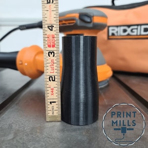 May include: A black 3D printed dust collection adapter for a sander, measuring 3 inches in height. The adapter is sitting on a wooden surface next to a measuring tape and a power tool.