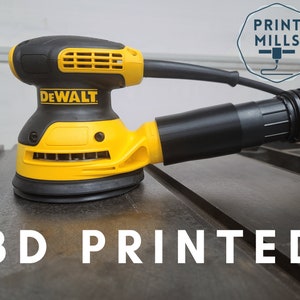 Puede incluir: Una lijadora DeWalt amarilla y negra con una manguera de recolección de polvo. La lijadora está sentada sobre una superficie de metal con el texto "3D PRINTED" en letras blancas.
