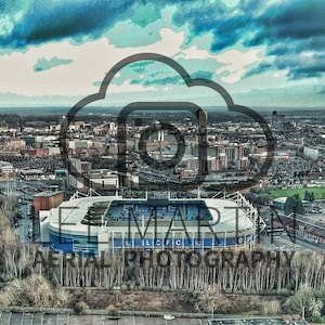 Puede incluir: Una vista aérea de un gran estadio con un exterior azul y blanco. El estadio está rodeado de árboles y un río. El horizonte de la ciudad es visible en el fondo.