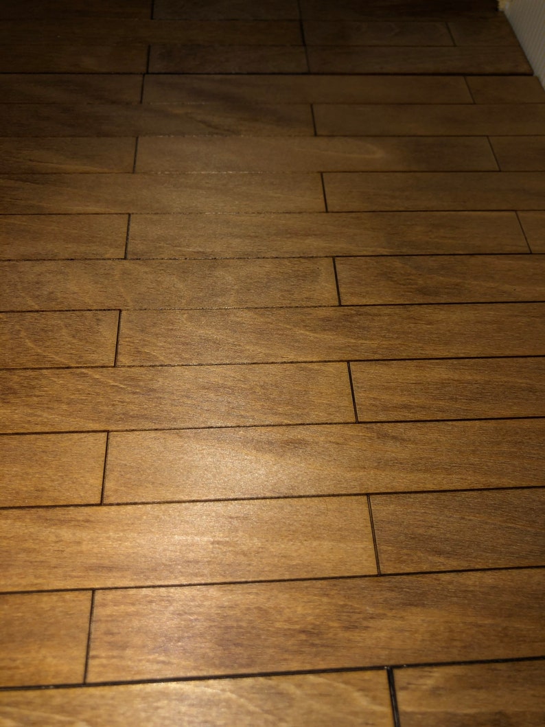 May include: Close-up of a wooden floor with a warm, brown tone. The floor is made of rectangular planks arranged in a parallel pattern. The wood grain is visible, adding texture and detail to the surface. The planks are separated by thin, dark lines.