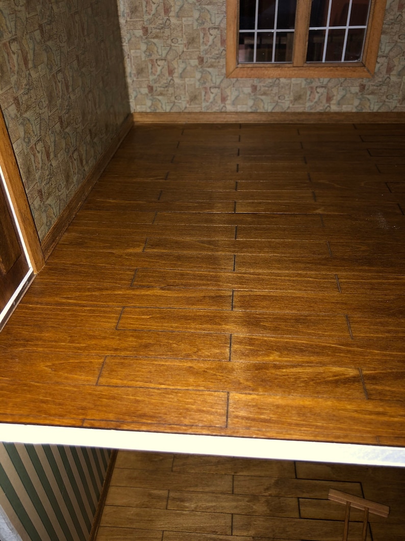 May include: A miniature dollhouse interior featuring a wooden floor with a warm, brown stain. The floorboards are rectangular and arranged in a staggered pattern. The walls are adorned with patterned wallpaper, and a window is visible in the background.