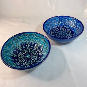 Puede incluir: Dos cuencos de cer&aacute;mica azul con intrincados dise&ntilde;os florales blancos y turquesa. Los cuencos son de tama&ntilde;os ligeramente diferentes y tienen un acabado brillante.