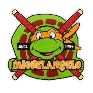 Könnte beinhalten: Ein grüner, orangefarbener und roter Teenage Mutant Ninja Turtles Charakter-Patch mit dem Namen "Michelangelo" und dem Text "Since 1984".