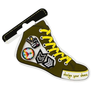 Könnte beinhalten: Ein grüner Canvas-Schuh mit gelben Schnürsenkeln und einer weißen Sohle. Der Schuh hat mehrere Patches, darunter ein Peace-Zeichen, eine Hand, die ein Peace-Zeichen macht, und ein Chevron-Muster.