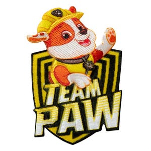 Könnte beinhalten: Gelber und schwarzer gestickter Aufnäher mit einem Cartoon-Hund, der einen gelben Bauhelm trägt, und dem Text "TEAM PAW"