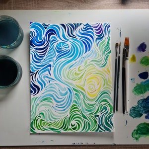 Op de afbeelding: Een aquarel schilderij van abstracte swirls in tinten blauw, groen en geel. Het schilderij is op een witte achtergrond en wordt omringd door kwasten en verfpotten.