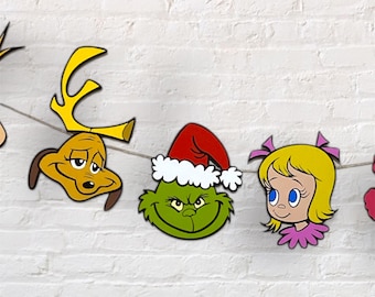 May include: A festive garland featuring cartoon character faces. The garland includes a yellow dog with antlers, a green face with a Santa hat, and a blonde girl with pink bows. The characters are strung on a thin, light-colored string.