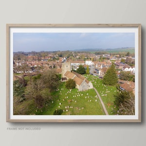 Puede incluir: Una vista aérea de un pequeño pueblo con una iglesia en el centro. La iglesia tiene un alto campanario y un techo marrón. El pueblo está rodeado de campos verdes y árboles.