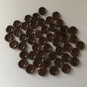 Op de afbeelding: Een verzameling bruine houten knopen met elk vier gaten. De knopen zijn in een cirkelvormige opstelling gerangschikt.