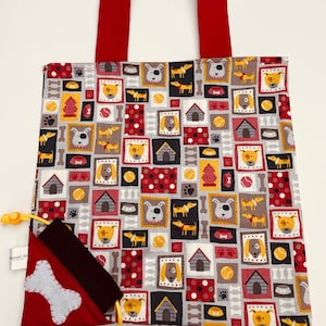 Peut inclure: Un sac fourre-tout rectangulaire avec une poignée rouge et une poche rouge assortie. Le sac présente un motif répété d'illustrations de chiens, de niches, d'os et de balles de tennis sur un fond gris. Une application d'os blanc est sur la poche rouge.