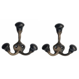 May include: Two antique-style black and gold metal hooks with three hooks each. The hooks have black ceramic knobs on the ends.
