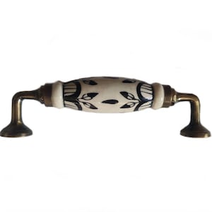 May include: A white ceramic cabinet knob with a black floral design and brass accents. The knob is oval shaped and has a slight curve to it.