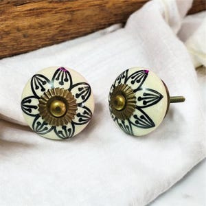 Può includere: Due pomelli in ceramica bianca con motivi floreali neri e dettagli dorati. I pomelli hanno una vite sul retro per il fissaggio ai mobili.