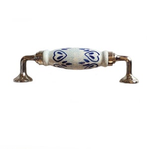 Puede incluir: Pomo de armario de cerámica blanca con un diseño floral azul y blanco y detalles en metal plateado.