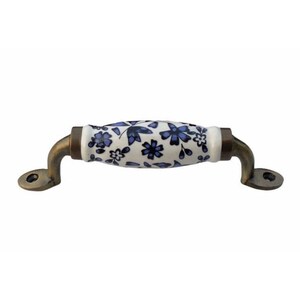Op de afbeelding: Een witte keramische kastknop met een blauw bloemenpatroon en antieke messing accenten. De knop heeft een afgeronde vorm en is ontworpen voor gebruik op kasten, lades of deuren.
