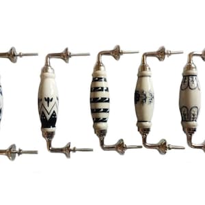 Peut inclure: Cinq boutons de cabinet en céramique avec une finition argentée et différents motifs bleus et blancs. Les boutons sont de forme ovale et ont un bras incurvé.