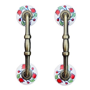 May include: Two antique-style cabinet pulls with a white ceramic base and a floral design featuring red and blue flowers. The pulls have a brass finish and a curved handle.