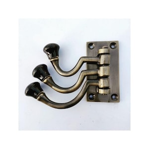May include: Antique brass coat rack with four hooks. Each hook has a black ceramic knob. The rack is mounted on a rectangular brass plate.