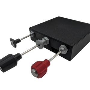 May include: A black rectangular electronic control box featuring three protruding metal rods. One rod has a small flat tip, one has a large black cylindrical knob, and one has a large red fluted knob, all secured with silver hexagonal nuts.