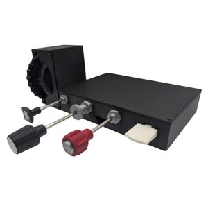 May include: A black rectangular control box featuring a side-mounted gear wheel, three protruding metal control rods with one black knob, one red knob, and one flat black tip, and a single white rectangular push-button switch on the front edge.