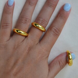 Puede incluir: Tres anillos de color dorado en una mano con esmalte de u&ntilde;as azul claro. Los anillos son de diferentes tama&ntilde;os y se llevan en diferentes dedos.