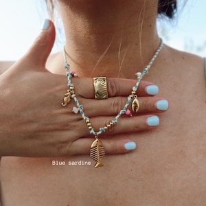 May include: A gold-toned necklace with a fish pendant, seahorse charm, and other decorative elements. The necklace is displayed with a gold ring. The text "Blue sardine" is visible in the image.