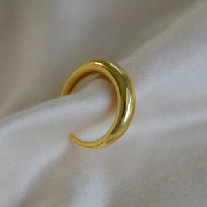 Puede incluir: Un anillo de media luna liso de color dorado. El anillo est&aacute; hecho de metal y tiene un acabado pulido.