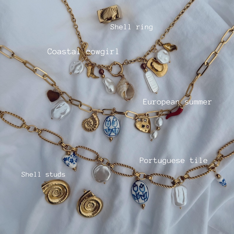 May include: A collection of gold-toned necklaces and shell studs with various charms, including pearls, a seashell ring, and pendants with the text "Coastal cowgirl", "European summer", and "Portuguese tile".