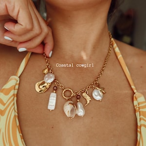 May include: Gold-toned charm necklace with a variety of pendants, including pearls, a boot, and a starfish. The necklace is worn against a yellow and orange patterned background. The text "Coastal cowgirl" is visible.