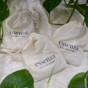 Puede incluir: Tres bolsas de algod&oacute;n blanco con cord&oacute;n de ajuste, con el texto "essenza jewelry store" impreso en cada una.