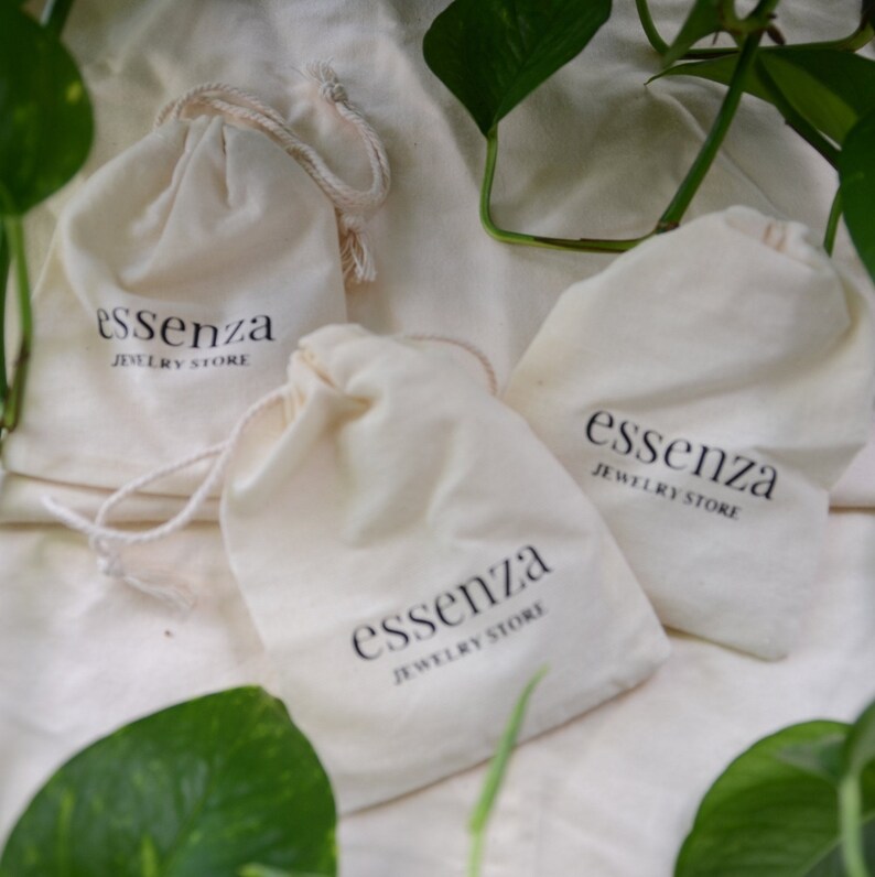 Puede incluir: Tres bolsas de algod&oacute;n blanco con cord&oacute;n de ajuste, con el texto "essenza jewelry store" impreso en cada una.