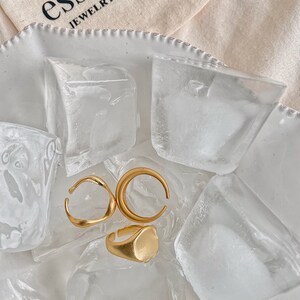 Puede incluir: Tres anillos de oro sobre un lecho de hielo. Los anillos son de diferentes formas, incluyendo un &oacute;valo redondeado, un semic&iacute;rculo y una banda curva.