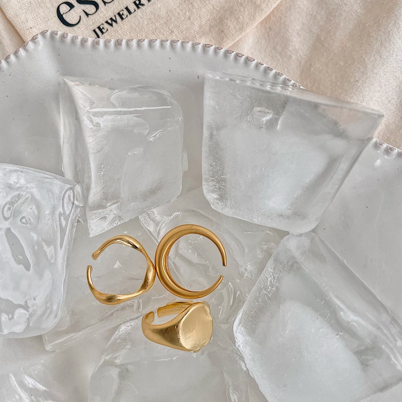 Puede incluir: Tres anillos de oro sobre un lecho de hielo. Los anillos son de diferentes formas, incluyendo un &oacute;valo redondeado, un semic&iacute;rculo y una banda curva.