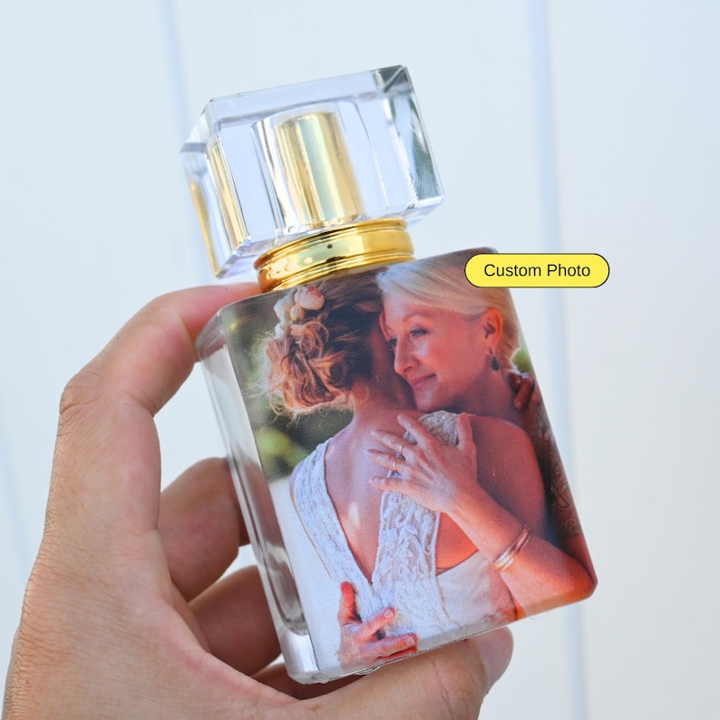 May include: A clear glass bottle with a gold cap and a custom photo of two people hugging. The photo is printed on the bottle and shows a woman in a white dress hugging another woman. The bottle is a personalized gift.