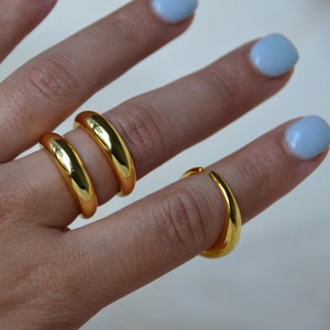 Puede incluir: Tres anillos de oro apilados en un dedo. Los anillos son todos lisos y tienen una forma redondeada.