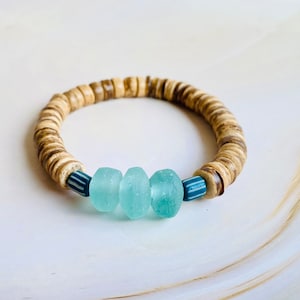 May include: A bracelet made of natural wood beads with three light blue glass beads and a dark blue and white striped bead.