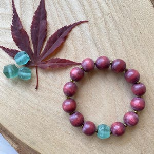 May include: A bracelet made of dark red wooden beads with a light green glass bead accent.