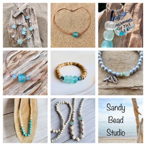 May include: A collection of handmade jewelry featuring sea glass and wood beads. The jewelry includes necklaces, bracelets, and a keychain. The jewelry is displayed on a wooden background with a beach theme. The text "Dreaming of the Sea" is on the keychain.